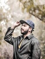 Portrait of a young man wearing a cap and jacket, confidently posing outdoors with a natural background photo