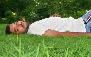 Man relaxing on the green grass in a peaceful park, gazing directly at the camera on a sunny day photo