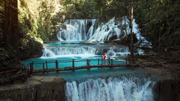 Cascade waterfalls with blue water and woman walking in bridge in Central Sulawesi, drone view video