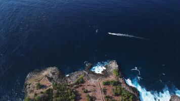 Rocky coastline with crashing ocean waves and sunshine with fog on Nusa Lembongan, drone view video