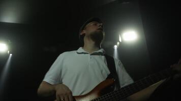 niedrig Winkel Aussicht von Bass Gitarrist spielen unter Bühne Beleuchtung. talentiert Mann durchführen beim Fall. er ist genießen Musical Show beim Nacht. video