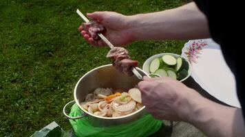 Professional chef preparing kebabs by stringing marinated meat pieces onto metal skewers, arranging sliced zucchini and onions alongside on rustic wooden surface in outdoor garden setting video