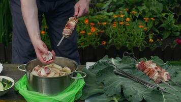Marinated pork meat and sliced onion are threaded onto skewers in preparation for outdoor barbecue grilling, showcasing culinary skills in a garden setting video