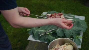Skillful cook marinating and adding sliced onions to seasoned meat skewers during outdoor barbecue preparation on wooden surface video