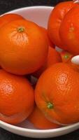 bright oranges tangerines stand in a white plate on a black table a hand picks up and puts oranges in a plate fruits video