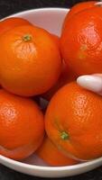 bright oranges tangerines stand in a white plate on a black table a hand picks up and puts oranges in a plate fruits video