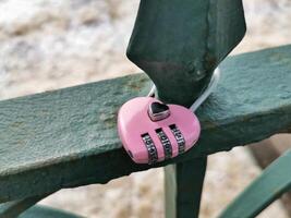 Close up view of a pink heart-shaped lock on a green bridge fence in a tranquil park. Wedding tradition. photo