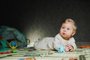 7-month-old baby is lying on a rug and playing. The child holds his head. A baby learns to crawl on the floor. A child in a beige romper. photo