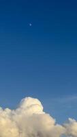 Minimalistic composition of crescent moon in deep blue sky above fluffy white clouds illuminated by sunlight. photo
