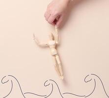 A wooden mannequin is pulled out of the water by a hand, depicted in the form of painted lines of waves. The concept of the image symbolizes help, support, rescue or overcoming difficult situations photo