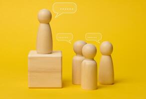 Wooden figures on a yellow background symbolize communication and leadership, one figure stands on a pedestal photo