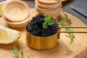 Black sturgeon caviar in copper bowl, lemon wedges and empty tartlets on table photo