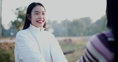 Handheld selective focus shot, Two Asian women in warm clothing happily stand and talk in the cold morning air. video