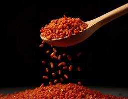 Falling red chili flakes from a wooden spoon on a black background. photo