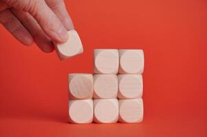 Placing wooden block on stacked cubes with red background photo