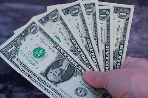 Hand holding multiple one dollar bills in a casual setting with dark background photo