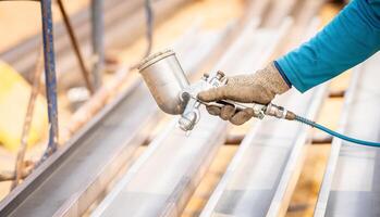 Construction worker painting a metal structure surface coating with a spray gun at construction site. Metal corrosion and rust protection. Industrial precision. Protective coating to metal structure. photo