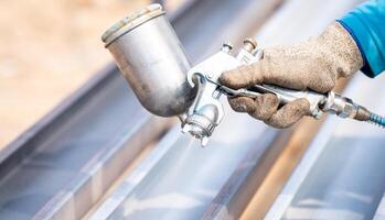 Construction worker painting metal structure surface coating with a spray gun at construction site. Metal corrosion and rust protection. Industrial precision. Protective coating to metal structure. photo