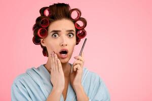 Shocked Woman With Curlers Talking On Cellphone Looking At Camera With Opened Mouth Posing Standing Over Yellow Studio Background, Wearing Dressing Gown. Mobile Communication, Shocking News photo