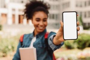 Black Student Girl Showing Smartphone Empty Screen Advertising Educational Mobile App For Cellphone Standing Outside. E-Learning Application For Students Concept. Mockup, Selective Focus On Phone photo