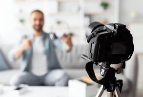 blogger recording review of wireless headphones at home, selective focus on modern dslr camera. Young vlogger showing modern device, giving feedback, promoting new gadget, copy space photo