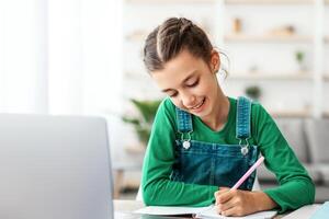 Happy girl student using laptop for distance education, doing homework or enjoying conference call, watching webinar tutorial, writing notes, studying with teacher, having virtual lesson photo