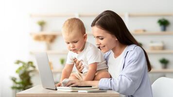 Young Smiling Woman Working On Laptop And Taking Care About Baby At Home, Freelancer Lady Spending Time With Infant Son And Using Computer, Enjoying Remote Job During Maternity Leave, Copy Space photo