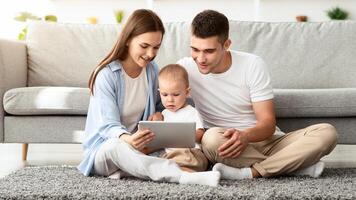 Family Leisure. Millennial Mom And Dad With Their Cute Toddler Son Using Digital Tablet Together At Home, Happy Young Parents Using Modern Gadget While Relaxing With Infant Child In Living Room photo