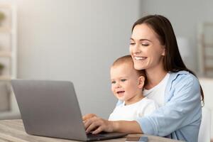 Portrait Of Happy Young Mother With Little Baby On Hands Using Laptop At Home Together, Smiling Millennial Mom Browsing Internet On Computer While Spending Time With Her Toddler Son, Copy Space photo