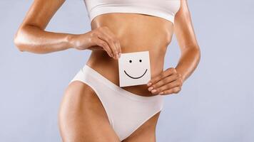 Love Yourself, Body Positivity And Care Concept. Closeup cropped view of unrecognizable slim woman holding paper post-it sticker note with smiley face over blue studio background, banner, panorama photo