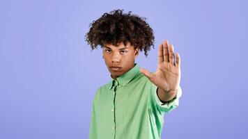 Serious black guy gesturing STOP, saying NO, showing rejection gesture, expressing refusal or denial, standing on blue studio background. Negative opinion concept photo