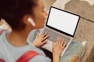 Unrecognizable African American Student Girl Using Laptop With Empty Screen Making Call Having Virtual Lecture Sitting Outside. Mockup, Selective Focus on Computer, Back View photo