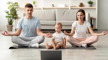 Online Yoga. Happy Young Family With Infant Child Meditating Together At Home With Laptop, Cheerful Parents Sitting In Lotus Position, Watching Tutorials On Computer, Enjoying Domestic Training photo