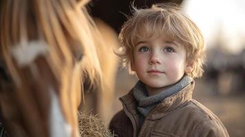 A young boy with tousled hair stands near a horse, holding a handful of hay. The warm light of late afternoon creates a peaceful atmosphere on the farm. photo