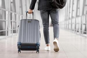 Unrecognizable Man With Bag And Suitcase Walking In Airport Terminal, Rear View Of Young Male On His Way To Flight Boarding Gate, Ready For Business Travel Or Vacation Journey, Cropped, Copy Space photo