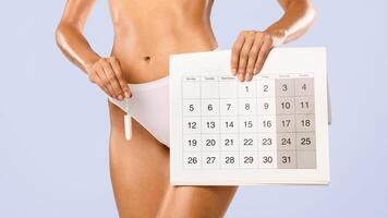 Menstrual Cycle And Intimate Hygiene Concept. Closeup cropped view of unrecognizable female in white panties holding absorbent tampon and paper calendar isolated on blue studio background, banner photo