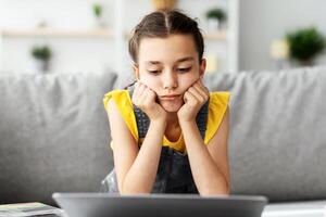 Boredom Concept. Sad Young Girl Sitting At Desk Using Laptop At Home, Looking At Computer Screen. Tired Upset Adolescent Having Problems, Watching Webinar, Distance Learning Concept photo