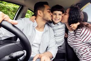 Loving Arabic Parents Kissing Their Little Son While Sitting In Car Together, Happy Middle Eastern Family Of Three Enjoying Summer Road Trip In New Automobile, Closeup Shot Inside Of Vehicle photo