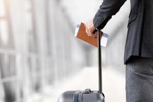 Air Travels Concept. Closeup Shot Of Man With Suitcase Holding Passport And Airline Tickets, Unrecognizable Male Traveller Waiting For Flight Boarding In Arport Terminal, Rear View, Cropped Image photo