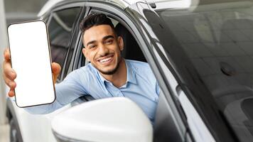 Cheerful arab man holding key from auto, buying brand new car in showroom. Happy middle-eastern guy buying new automobile, sitting inside black car and showing automatic key at camera, smiling photo