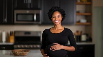 A smiling woman stands in a kitchen, cradling her baby bump. The modern space is warmly lit, reflecting a serene atmosphere. She enjoys this beautiful phase of her life with happiness. photo