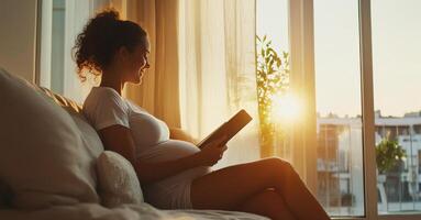 A pregnant woman sits comfortably on a sofa, enjoying a book as the warm sunlight streams through the window, creating a serene and cozy atmosphere at home during sunset. photo