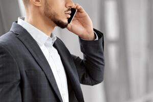 Mobile Call. Young Arab Businessman Talking On Cellphone At Airport Terminal, Unrecognizable Middle Eastern Entrepreneur Having Phone Conversation While Waiting For Flight, Side View, Cropped Shot photo
