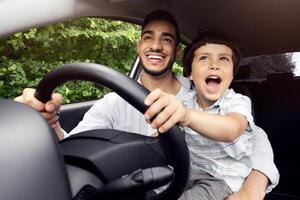 Portrait Of Excited Little Boy Driving Car With His Arab Dad, Holding Steering Wheel And Laughing, Caring Middle Eastern Father Teaching Son How To Drive, Enjoying Road Trip In Modern Vehicle photo