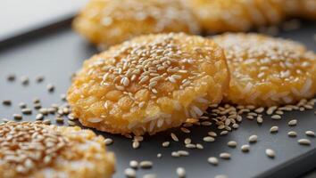 Close up view of golden fried rice cakes topped with white sesame seeds on display. photo