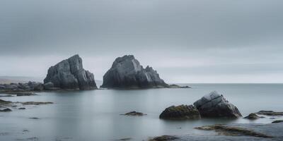 Rocks emerging from the ocean under overcast skies create a stark and moody coastal landscape near an unknown shore. photo