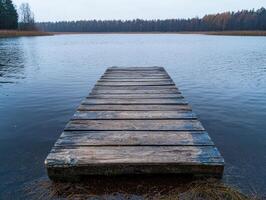 Wooden dock extending into a calm lake, surrounded by autumn trees photo