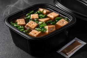 Delicious tofu soup in a black container with green onions photo