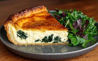 A slice of spinach and feta quiche on a plate with a side salad photo