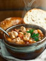 A hearty bowl of stew with chunks of meat and beans, served with crusty bread photo